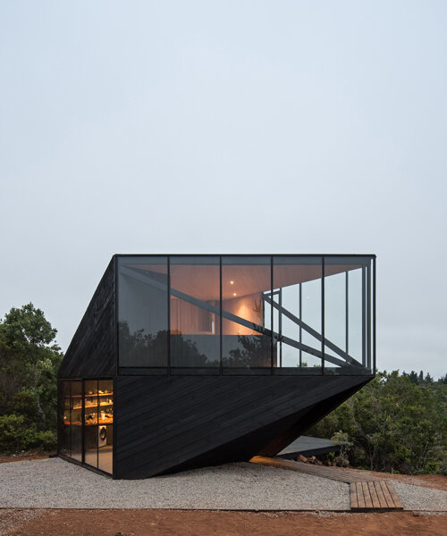 la cabaña revestida de madera negra de 2DM apunta hacia el mar en la costa chilena