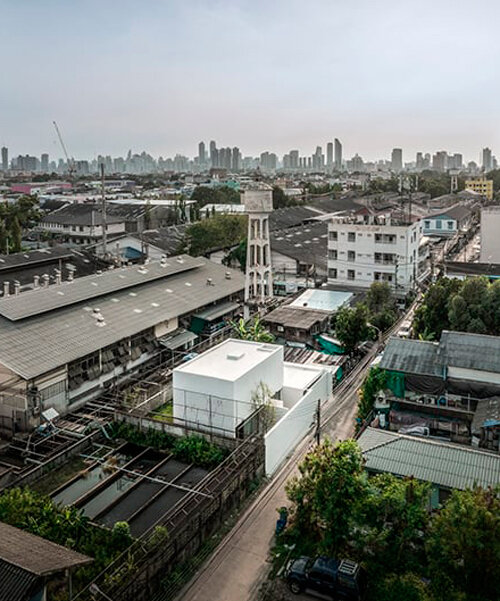 un denso bloque geométrico color blanco surge de un barrio urbano de bangkok