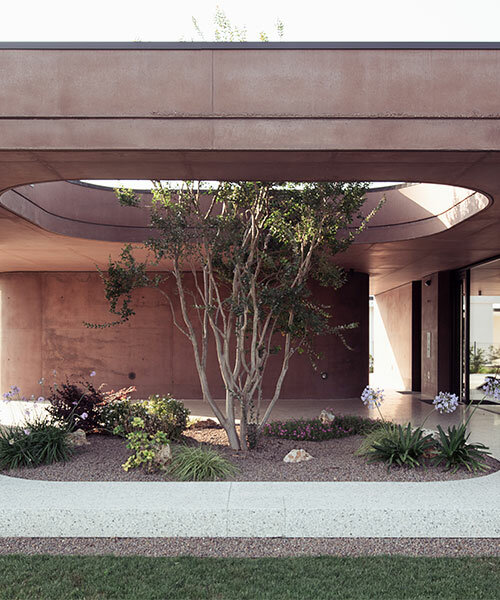 la casa de concreto rosa de MIDE architetti se curva alrededor de una abundante vegetación en italia